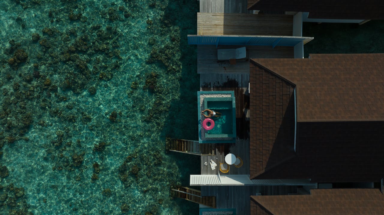 services-02 Stunning aerial view of a Maldives overwater villa with clear lagoon, featuring a bright pool float.